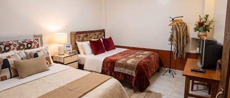 A hotel room with two beds, a TV, a desk with a computer, a wardrobe, and a bathroom.
