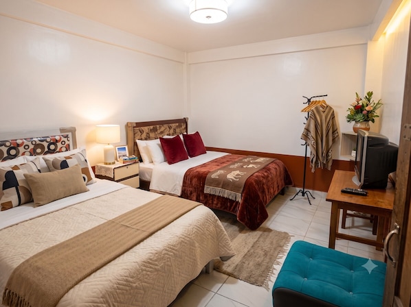 A hotel room with two beds, a TV, a desk with a computer, a wardrobe, and a bathroom.