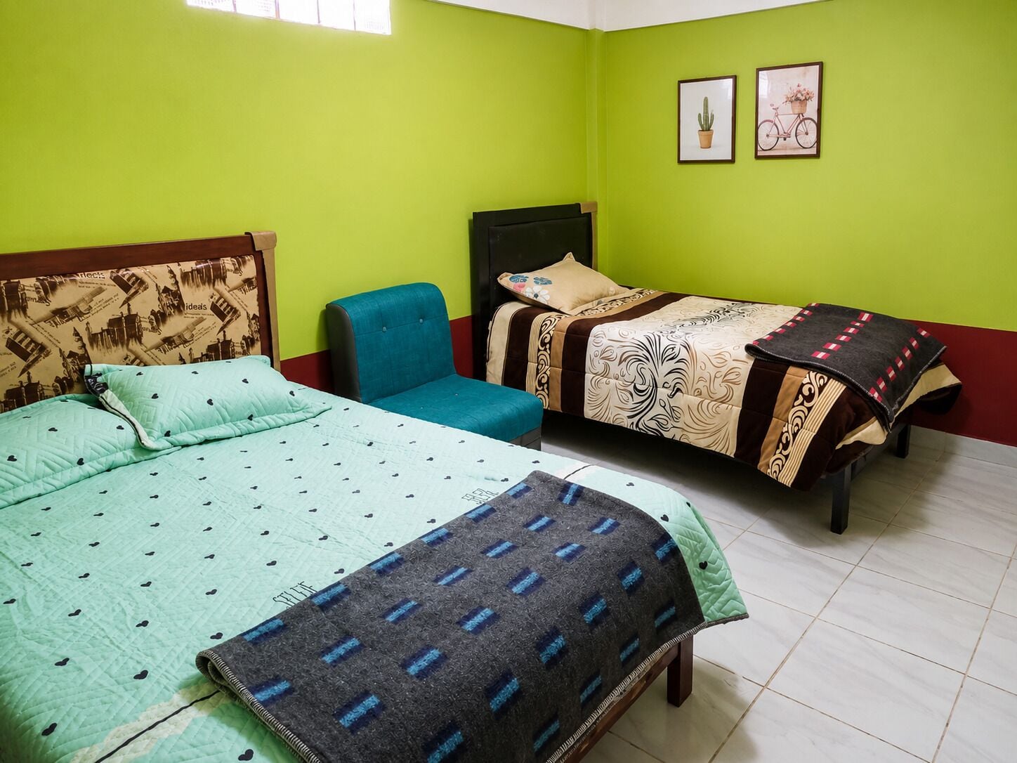 A room with two beds, a chair, and two framed pictures on the wall.