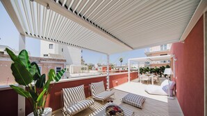 Eine Dachterrasse mit überdachter Lounge, einem Esstisch und Kübelpflanzen.