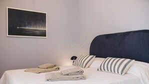 Ein ordentlich bezogenes Bett mit gefalteten Handtüchern, einem dunklen Kopfteil und einem gerahmten Bild an der Wand.