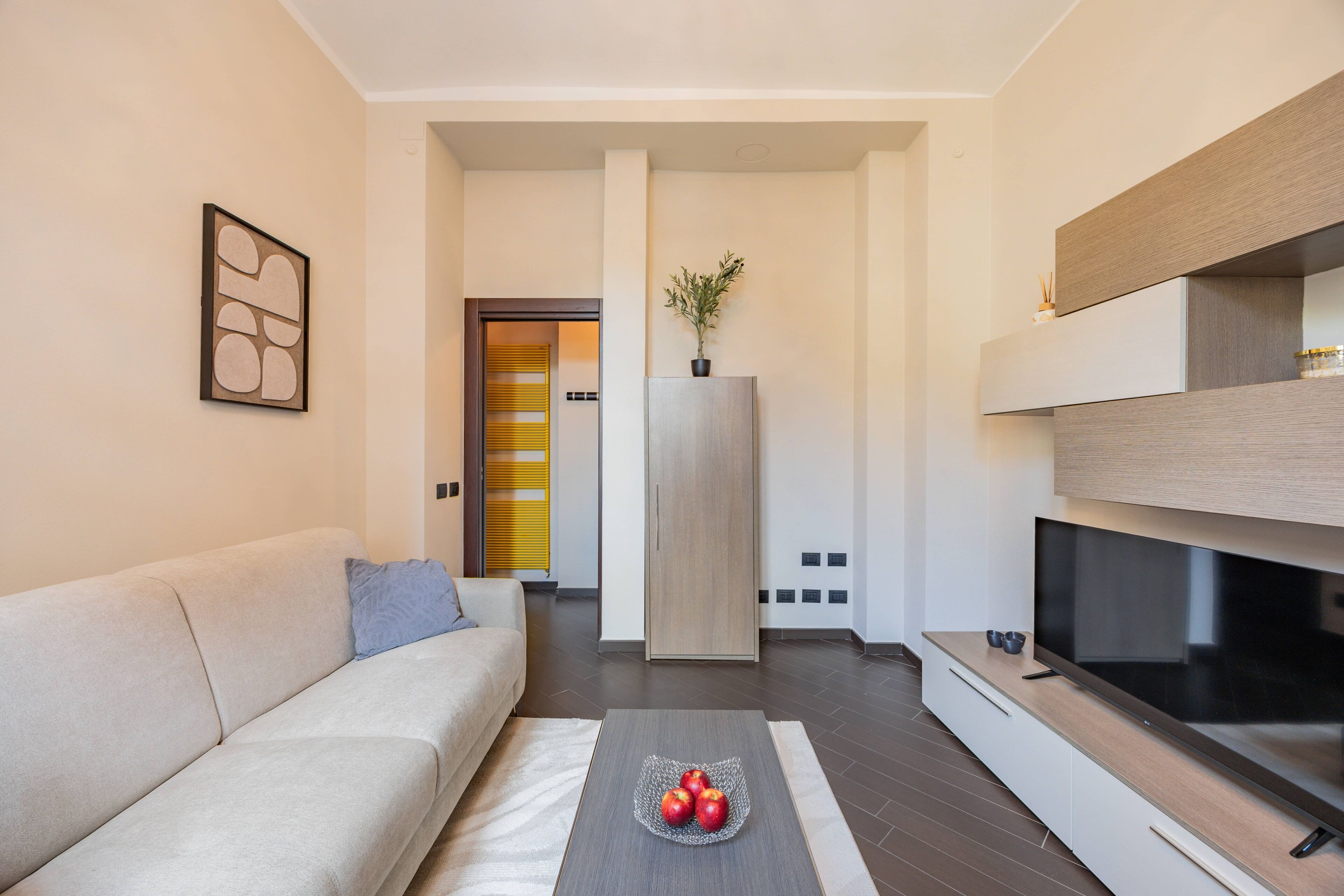 A modern living room with a sofa, a coffee table with fruit, a TV, and a minimalist decor.