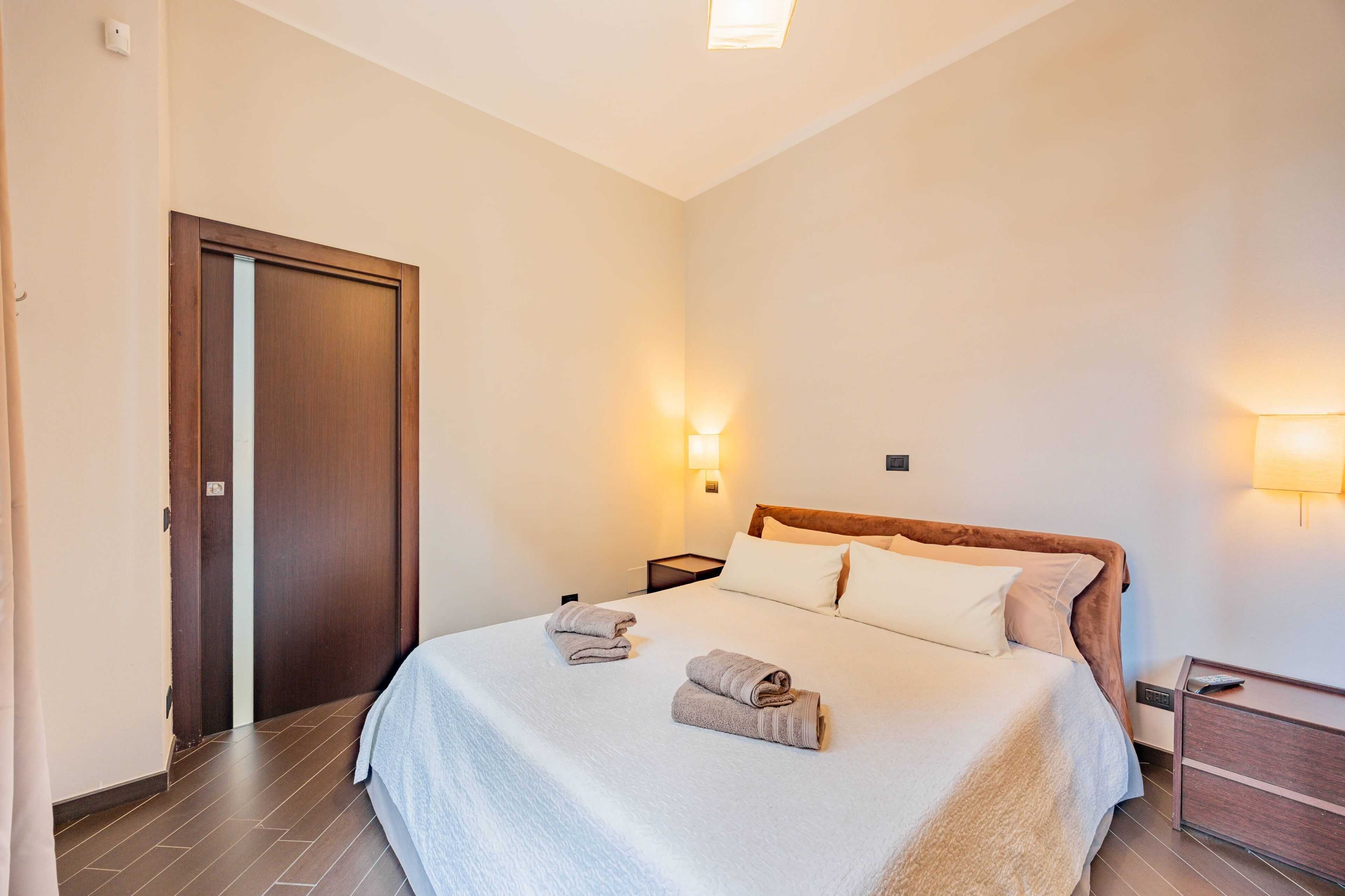 Une chambre d’hôtel avec un lit, deux lampes de chevet, une porte en bois et une table de chevet.