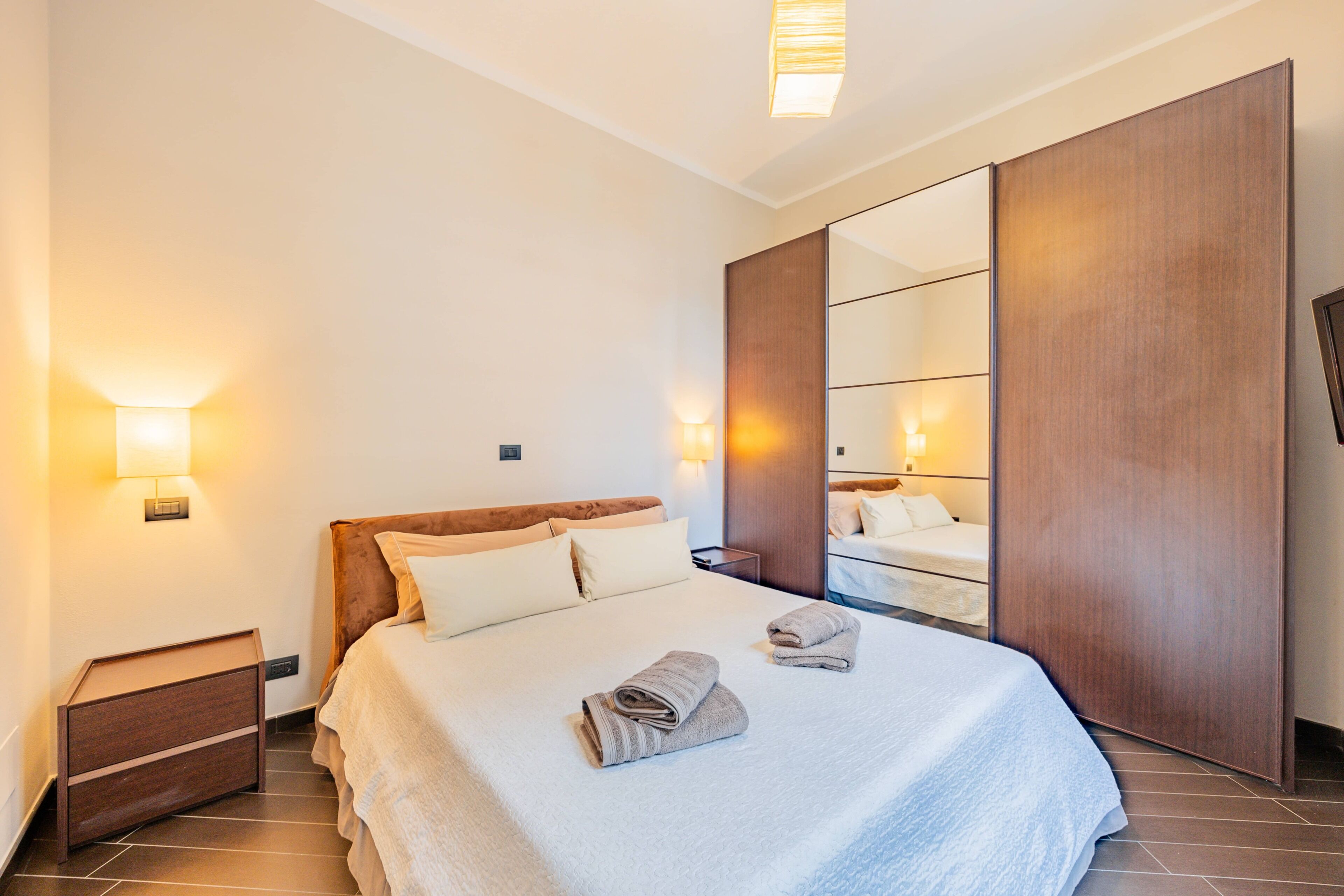 A hotel room with a large bed, bedside lamps, a wooden wardrobe, and a mirror.