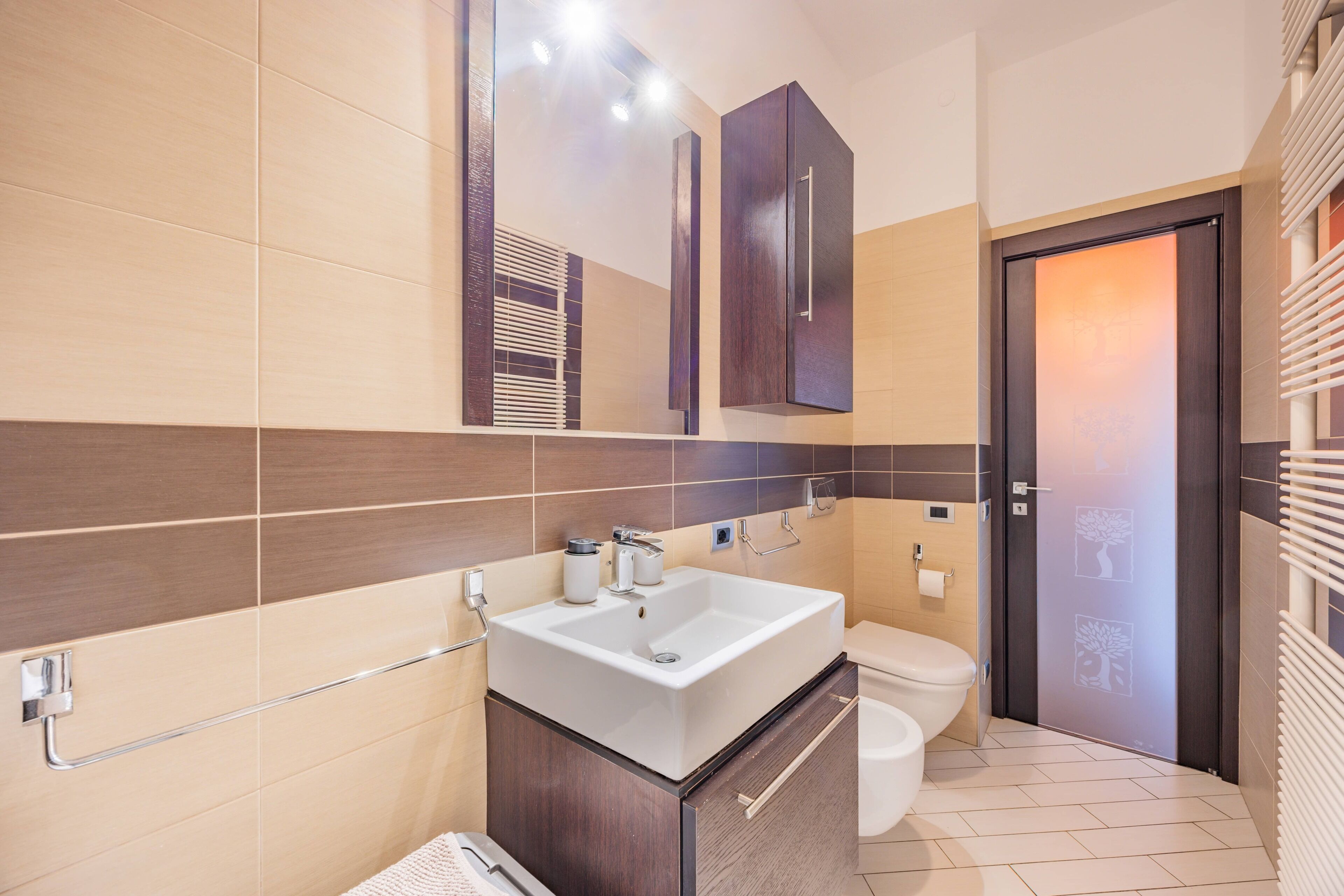 Une salle de bain moderne avec un grand miroir, un lavabo blanc, des toilettes et un espace douche.