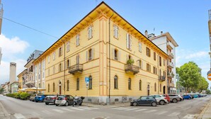 Ein gelbes Gebäude mit mehreren Balkonen, abgestellten Autos und blauem Himmel.