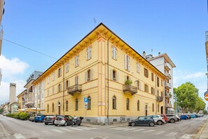 A yellow building with multiple balconies, parked cars, and a clear blue sky. - Eleven Maison [Centro Cuneo zona sferisterio] (Cuneo)