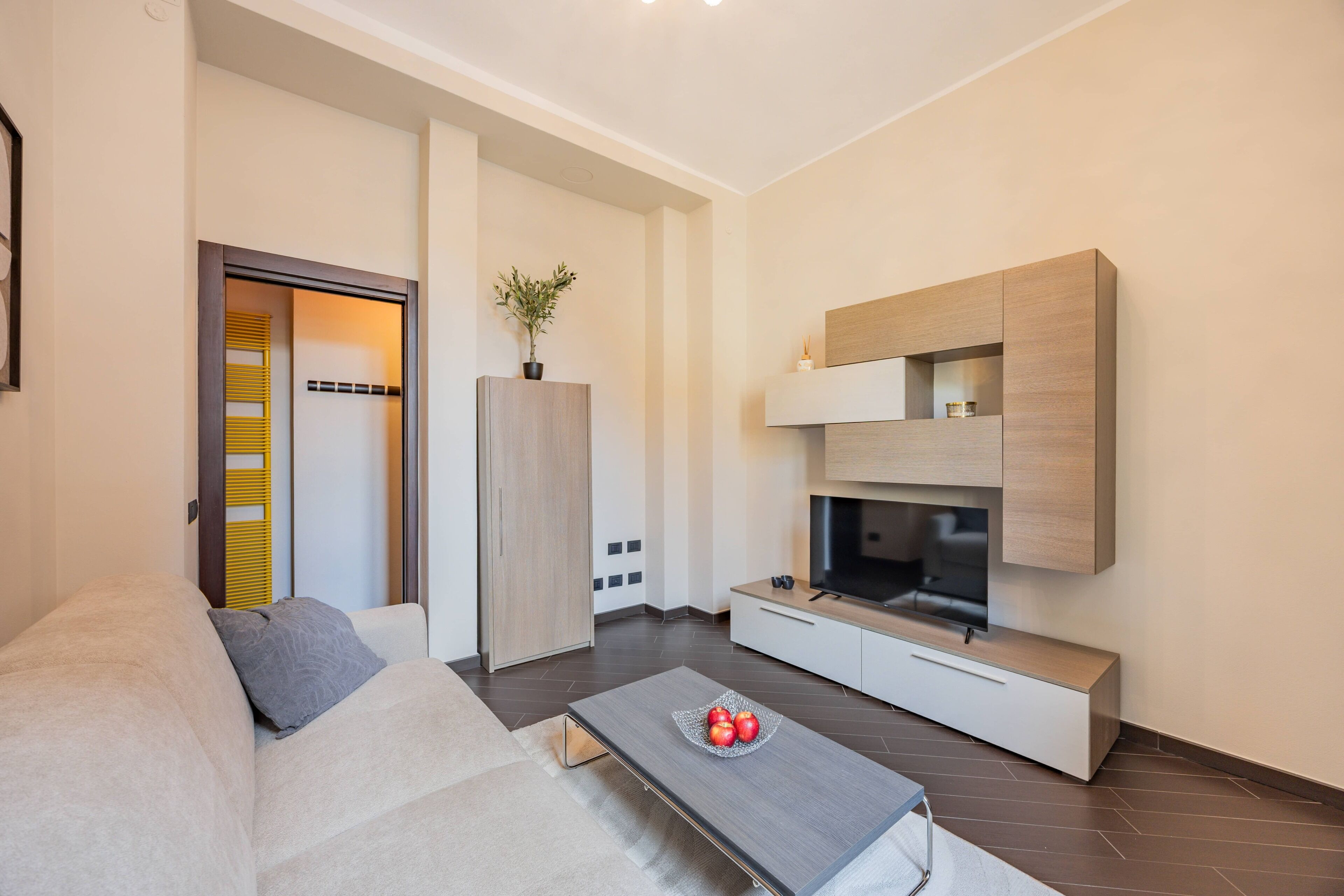 Een moderne woonkamer met een bank, een salontafel met fruit, een televisie en een minimalistische kast.