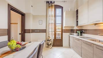 Een moderne keuken met een eethoek, met een tafel met een fruitmand, een keukeneiland en uitzicht door een deur.