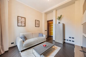 A modern living room with a sofa, a coffee table with apples, and abstract wall art. - Eleven Maison [Centro Cuneo zona sferisterio] (Cuneo)