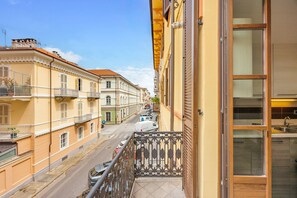 Balcón con baranda metálica que da a una calle con coches aparcados y edificios.