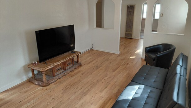 Una sala de estar con televisor de pantalla plana sobre un mueble de madera, sofá de cuero negro y piso de madera.