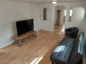 Ein Wohnzimmer mit einem Flachbildfernseher auf einem Holzständer, einem schwarzen Ledersofa und Holzböden.