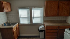 Una cocina con armarios de madera, un lavamanos, una ventana con persianas, un cesto de basura y una estufa.