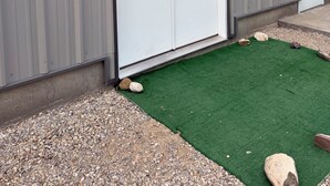 Ein Gebäude mit einer weißen Doppeltür, einem kleinen Kiesgrundstück und einem Streifen grüner Kunstrasen.