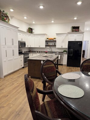 A modern kitchen with white cabinetry, a central island, and a dining area with round tables and patterned chairs. - Spacious Loft,  Sleeps 4, 2 QueenBeds,  gourmet kitchen, RV PKG, Newly Updated. (Vernal)