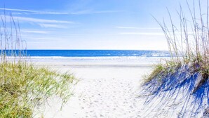 Une plage de sable blanc, un ciel bleu azur et l’océan.