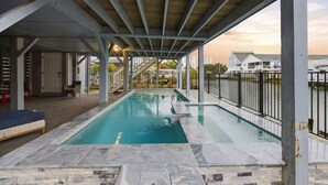 Une piscine extérieure dotée d’un espace couvert, d’une terrasse carrelée en pierre et offrant une vue sur les immeubles résidentiels.