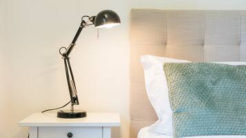 Yöpöytä, jossa on lamppu, kuviollinen päätyosaan varustettu sänky ja teksturoidulla päällisellä varustettu tyyny.