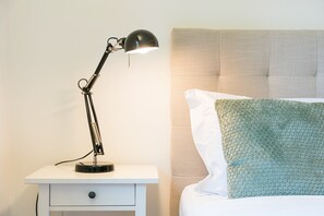 A bedside table with a lamp, a bed with a patterned headboard, and a pillow with a textured cover. - GuestReady - Quinta do Outeiro (Anadia)