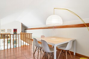 A dining area with a wooden table, white chairs, a white pendant light, and a staircase with wooden railings. - GuestReady - Quinta do Outeiro (Anadia)