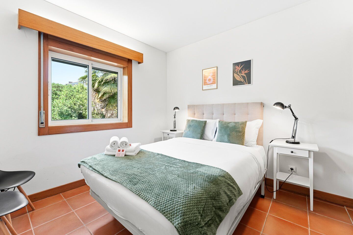 A bedroom with a bed, two bedside tables, a window with a view, and a chair.