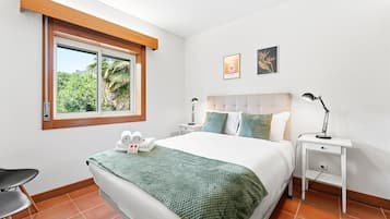 A bedroom with a bed, two bedside tables, a window with a view, and a chair.