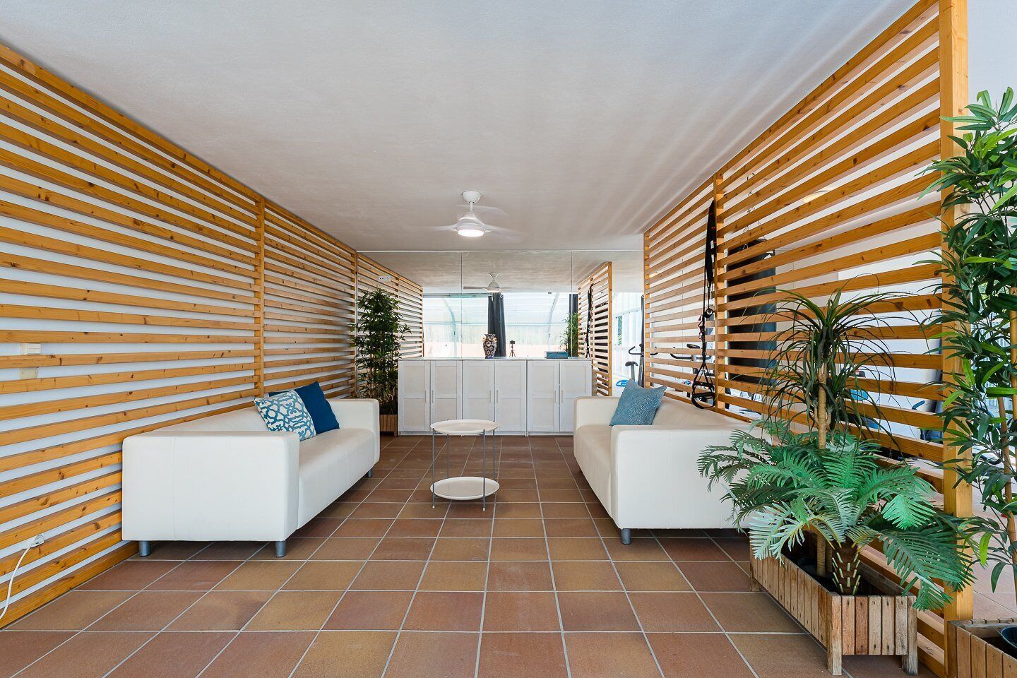 Un interno moderno con pareti in listelli di legno, divani bianchi, un tavolo rotondo al centro e piante in vaso.