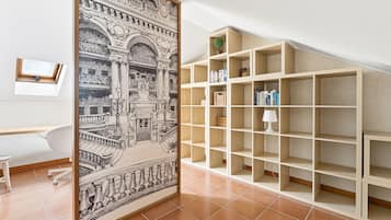 A room with a large framed black and white architectural print, a white desk, a chair, and a wooden bookshelf with books and a lamp.