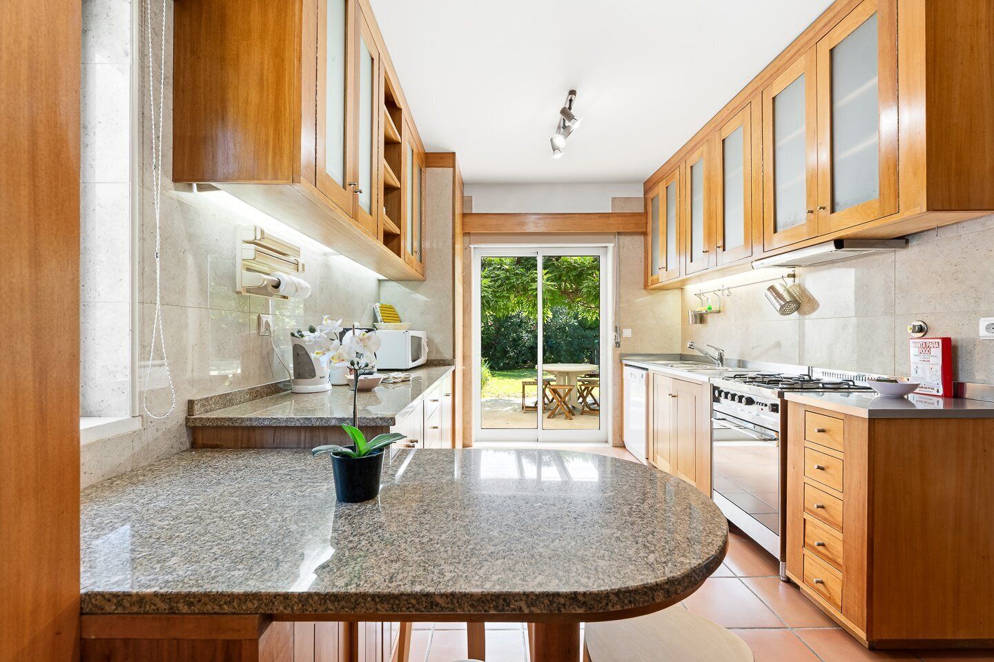 Una cocina con armarios de madera, encimera de granito, estufa y vistas al exterior.