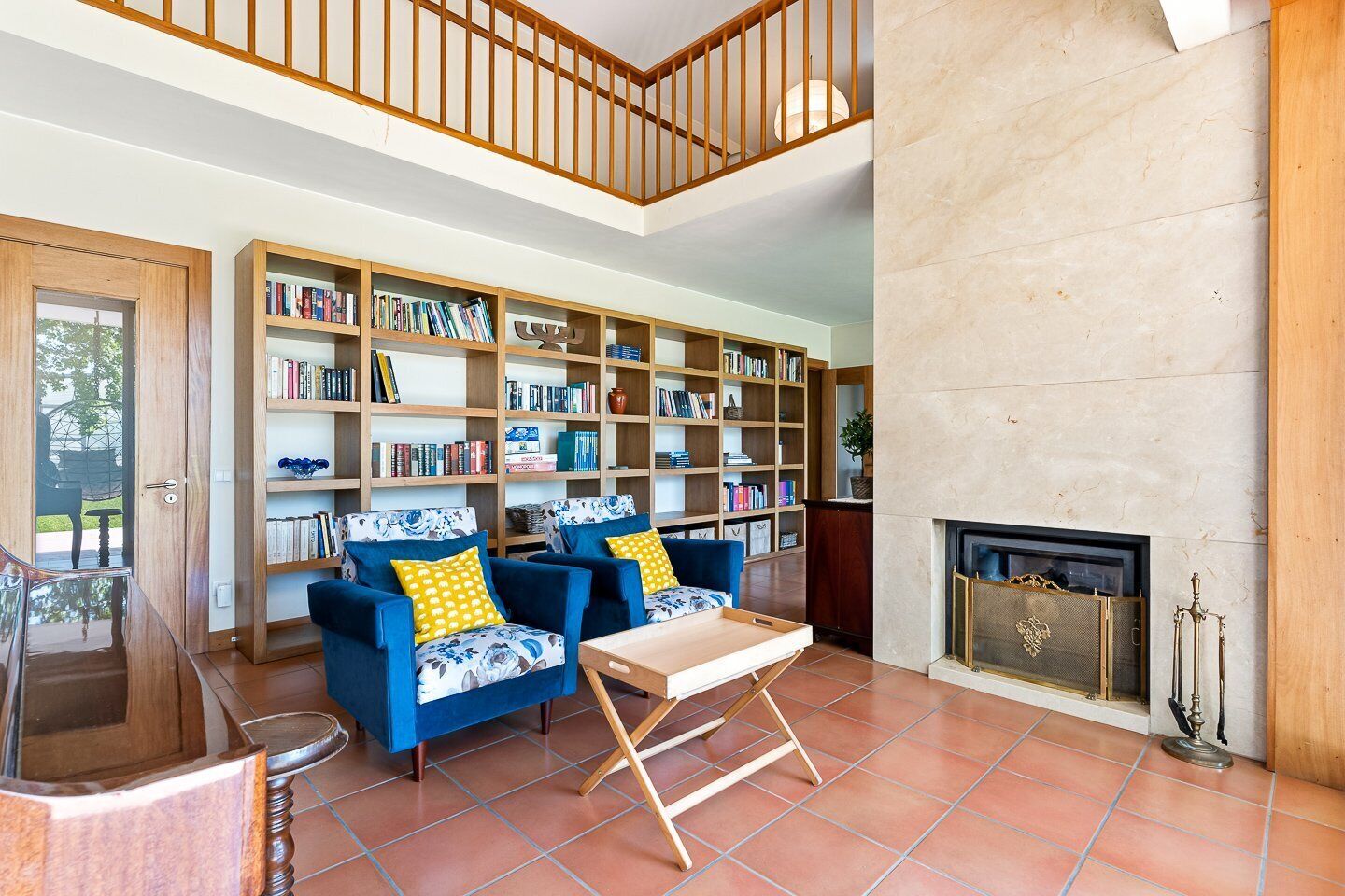 Ein geräumiges Wohnzimmer mit hoher Decke, einem Kamin und einer großen Bibliothek voller Bücher.