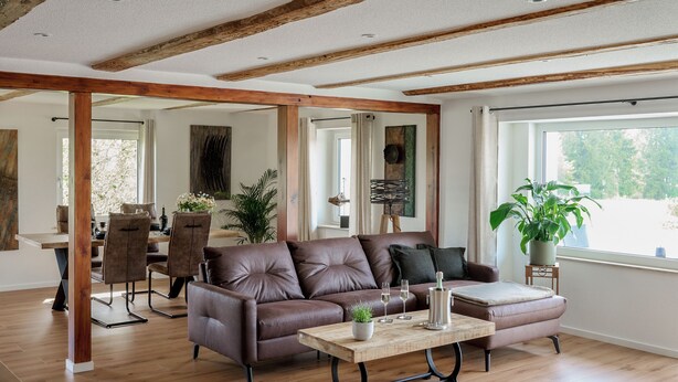 A spacious living area with a brown leather sofa, a wooden coffee table, and a dining area with a wooden table and chairs.