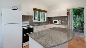 A modern kitchen with white cabinets, a granite countertop, a stove, a microwave, and a window with a view of greenery. - Welcome to Caversham Townhouse (Arcadia)