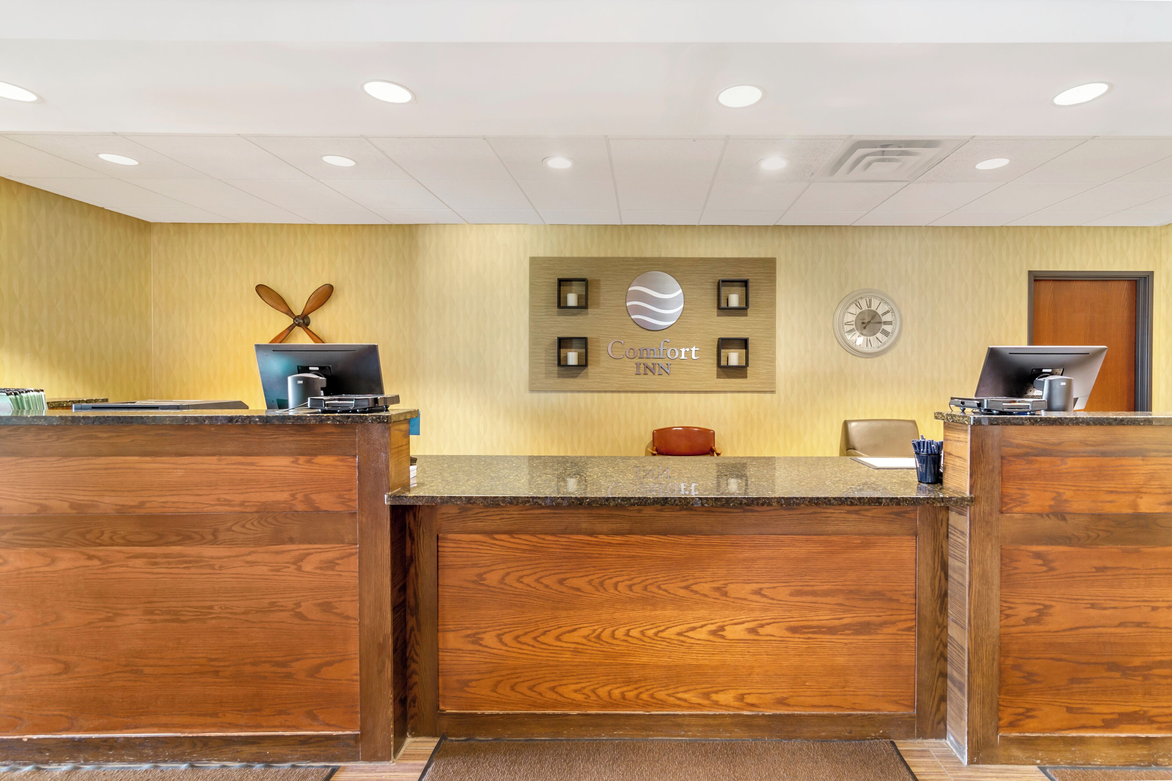 A hotel reception desk with a wooden finish, a clock, and a sign that reads 'Comfort Inn.'