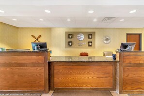 A hotel reception desk with a wooden finish, a clock, and a sign that reads 'Comfort Inn.' - Legend Hotel Minot (Minot)