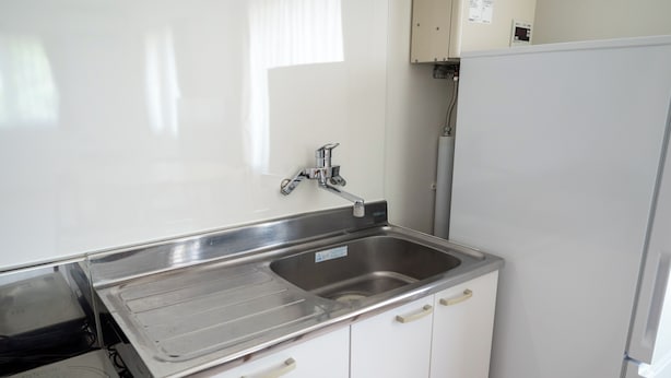 Een keuken met een roestvrijstalen spoelbak, een inbouwoven en witte keukenkastjes.