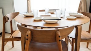 Una mesa de comedor redonda de madera con platos, cuencos y tazas blancos, rodeada de sillas de madera.