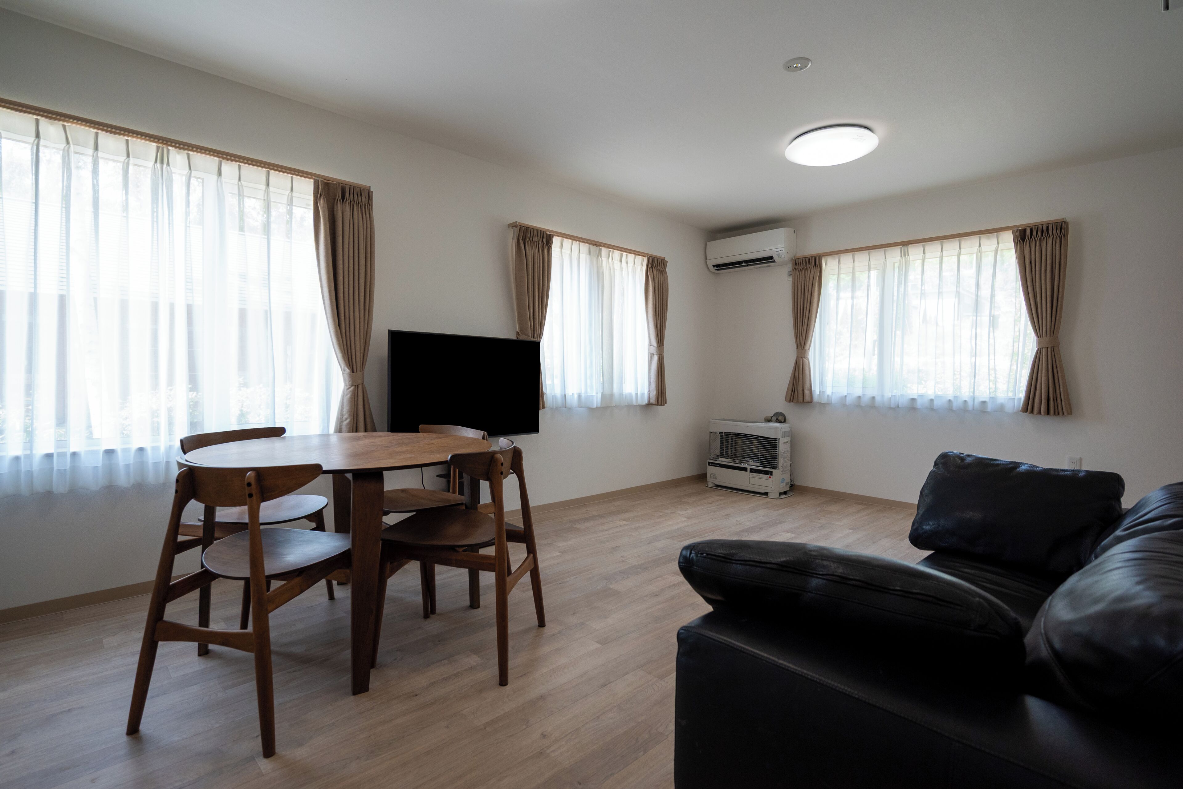 A room with a wooden dining table, chairs, a black leather sofa, and a flat-screen TV.