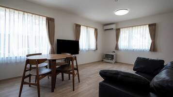 A room with a wooden dining table, chairs, a black leather sofa, and a flat-screen TV.