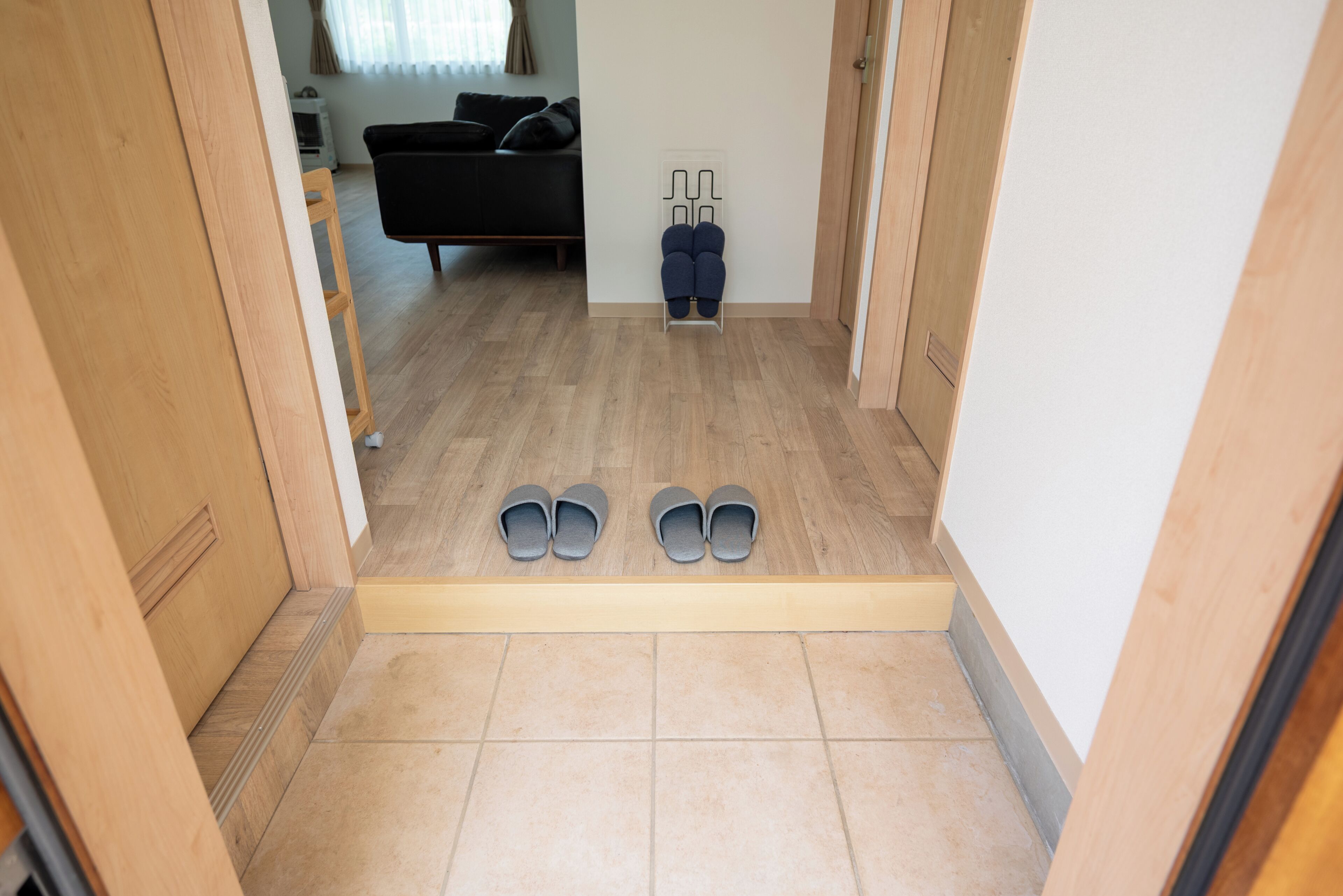 A hallway with a wooden floor, a pair of shoes on a shoe rack, and a black sofa in the background.