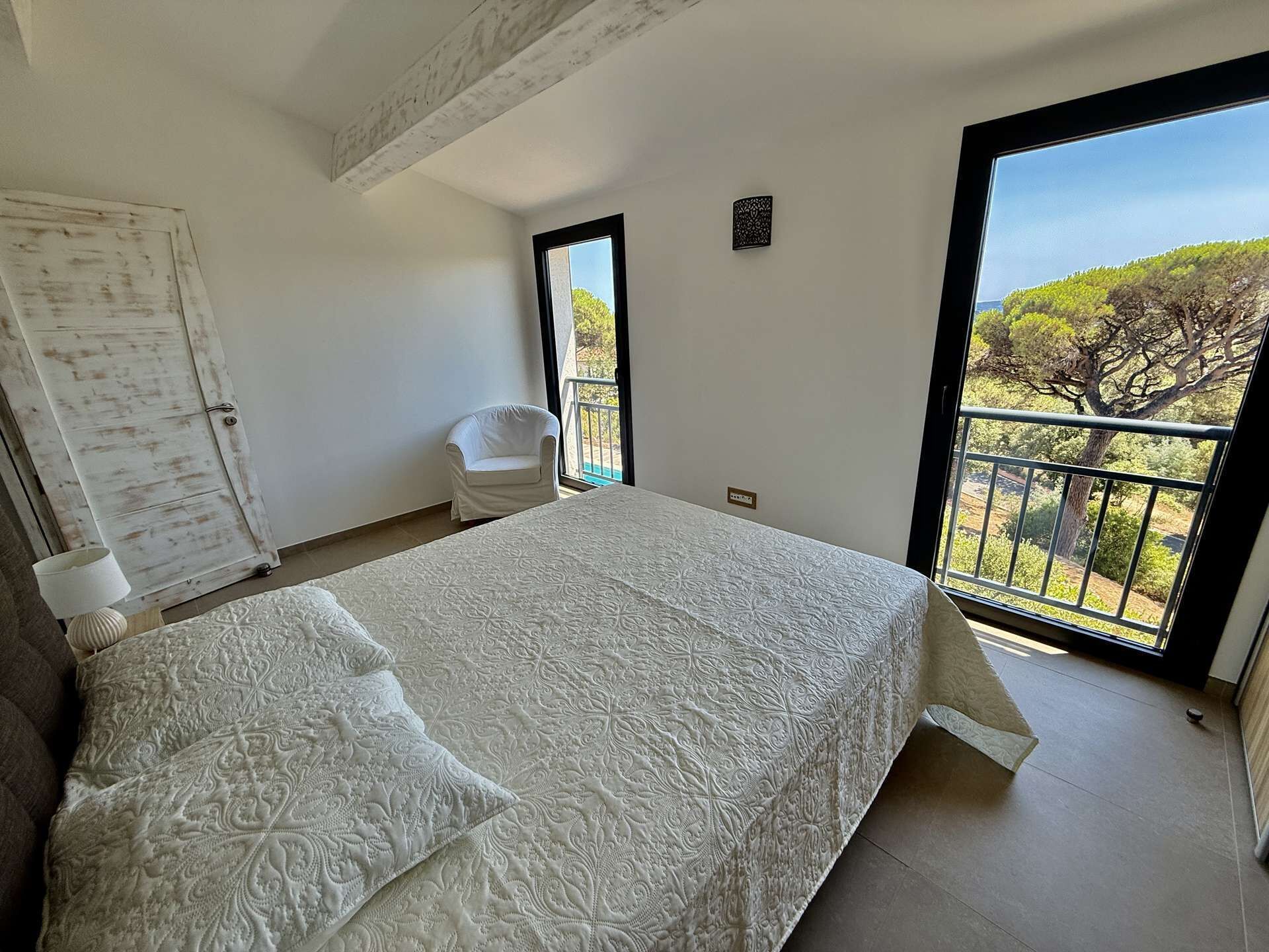 A bedroom with a large bed, a chair, a wardrobe, and a balcony with a view.