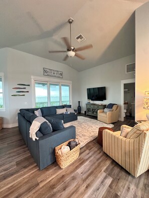 A spacious living room with a dark grey sofa, a striped armchair, and a ceiling fan.