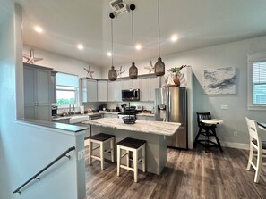 A modern kitchen with grey cabinets, a central island, pendant lights, and a refrigerator.