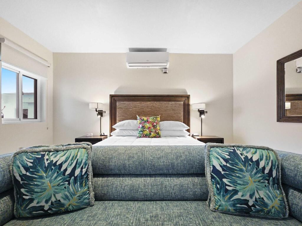 Quarto de hotel com uma cama, duas mesas de cabeceira, uma janela e um espelho.