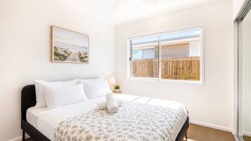 Ein Schlafzimmer mit einem Bett, einem Deckenventilator, einem Fenster mit Blick auf einen Holenzaun und einem gerahmten Bild an der Wand.