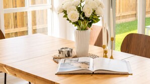 A dining table with a vase of white flowers, an open book, and candle holders. - Haus Verde | 4BR Greenbank Hideout in Logan (Greenbank)