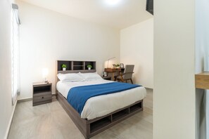 Une chambre à coucher comprenant un lit, une table de chevet, une lampe, un bureau, une chaise et une petite plante.