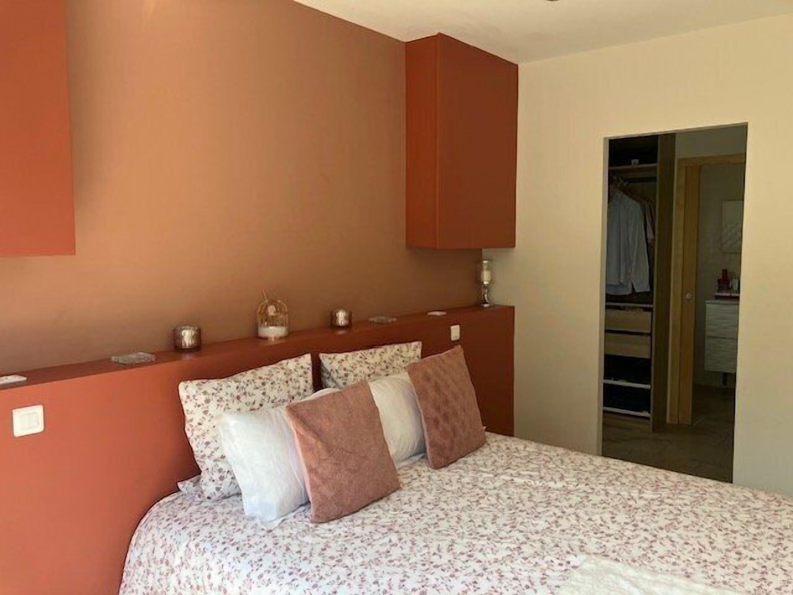 A bedroom with a bed, pillows, a nightstand, a mirror, and a wardrobe.