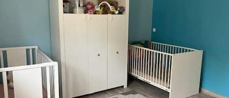 Une piĂšce avec deux berceaux blancs, une armoire blanche et un mur bleu.