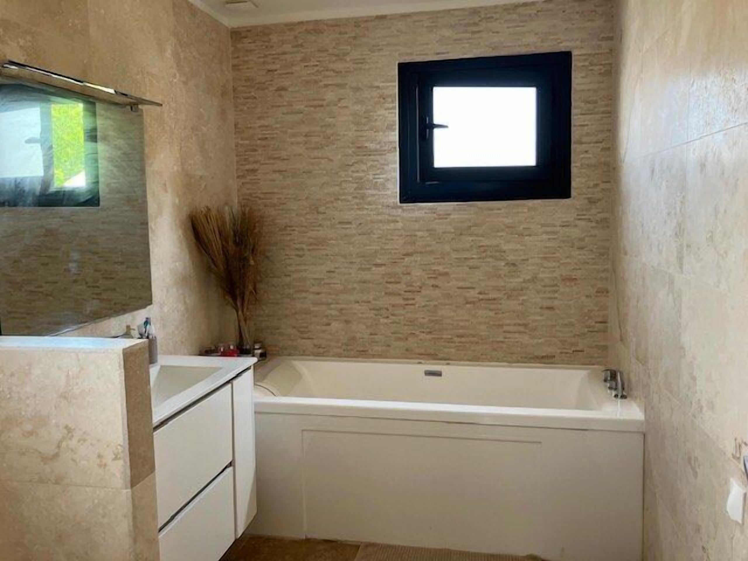 A bathroom with a bathtub, a mirror, and a window.
